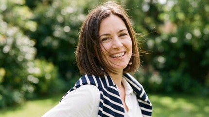 Naklejka premium Smiling young woman portrait outdoors in natural light with short brown hair and striped sweater, happy casual lifestyle close-up showing bright smile and fresh spring atmosphere