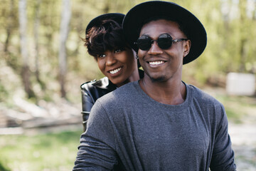 Obraz premium African American couple embracing, both wearing hats, posing and smiling outdoors with a natural background