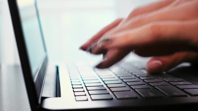 Closeup of female hands typing on laptop keyboard. Macro view of fingertip movement and key detail of remote tutor preparing lesson content and composing messages. Woman is working on computer
