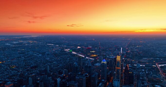 Vast metropolis panorama against splendid orange sky. Drone descending slowly over the high-rise downtown of Philadelphia, Pennsylvania at dusk time.
