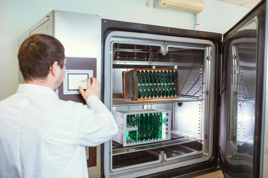 Engineer programs, sets up a test laboratory for finished printed circuit boards. Warm-cold test chamber with printed circuit boards installed during testing.