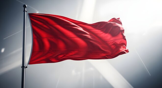 A vibrant red flag waving in the wind against a bright overcast sky