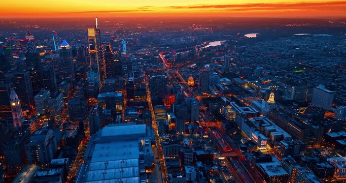 Spectacular luminous streets with bright city lights at sunset time. Scenery of Philadelphia, Pennsylvania against orange sky from drone.
