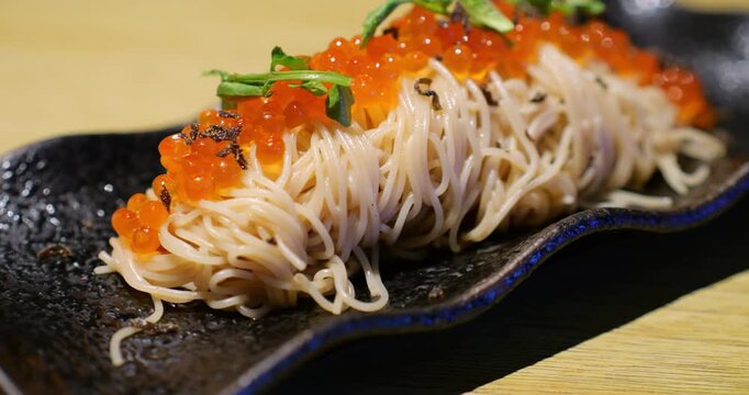 Gourmet somen noodles glistening with ikura and delicate black truffle shavings, showcasing elegant Japanese culinary craftsmanship on a sleek black plate. Slow motion shot of prepared meal