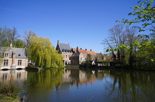 Blick aus Richtung Beginenhof auf das gegen&uuml;berliegende Ufer des Minnewater vor blauem Himmel im Sonnenschein. im Fr&uuml;hling in der Altstadt von Br&uuml;gge in Westflandern in Belgien