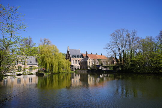 Blick aus Richtung Beginenhof auf das gegen&uuml;berliegende Ufer des Minnewater vor blauem Himmel im Sonnenschein. im Fr&uuml;hling in der Altstadt von Br&uuml;gge in Westflandern in Belgien