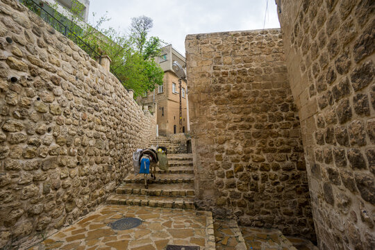 A donkey carrying goods walks through narrow stone streets of the historic city of Mardin. The scenes reflect traditional transportation methods and daily life among the old stone architecture of sout