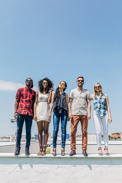 Diverse friends standing together on rooftop in sunshine