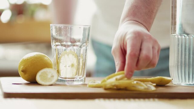 Preparing Fresh Lemon Water: Man's Hand Dropping Fruit and Pouring Mineral Water 4K
