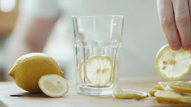 Preparing Fresh Lemon Water: Man's Hand Dropping Fruit and Pouring Mineral Water 4K