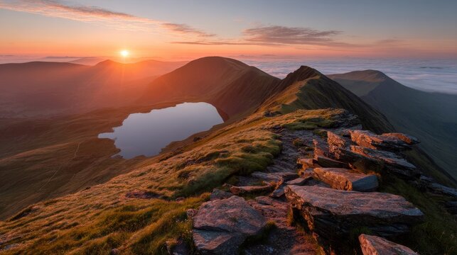 Stunning orange-yellow sunrise from Sharp Edge on Blencathra in Lake District, with reflections in a mountain tarn and a cloud inversion rolling over distant peaks.