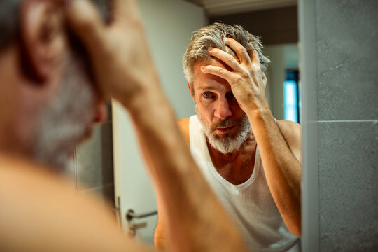 Concerned middle-aged man checking reflection in bathroom mirror