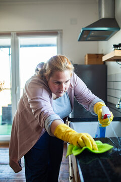 Woman cleaning kitchen countertop at home with spray and cloth