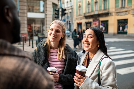 Two women friends chatting with takeaway coffee on a city street