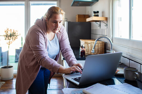 Woman working on laptop in home kitchen