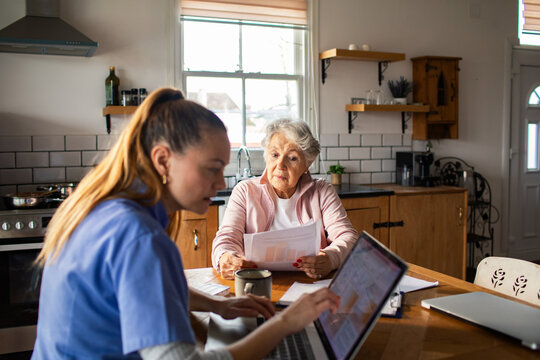 Caregiver assisting senior with paperwork at kitchen table
