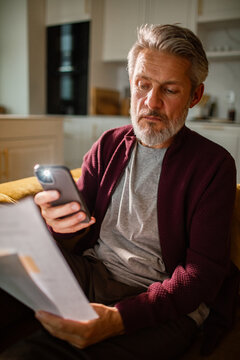 Mature man checking bills on smartphone at home