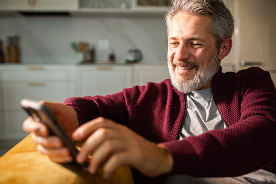 Smiling middle-aged man using smartphone on sofa at home