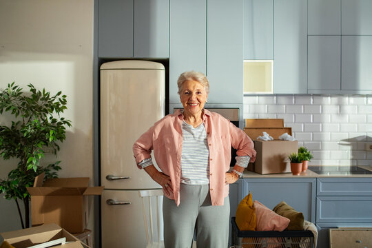 Smiling senior woman standing in modern kitchen with moving boxes