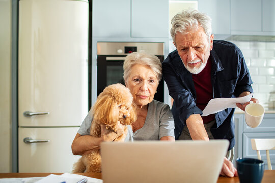 Senior couple reviewing finances on laptop in kitchen