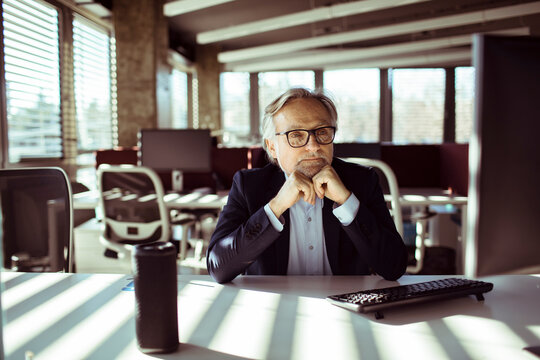 Senior businessman thinking at computer in modern office