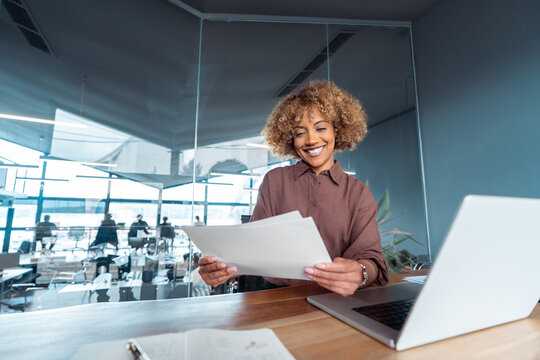 Focused African American business woman working on laptop computer reading financial document report in office. Happy accountant entrepreneur manager businesswoman doing paperwork using pc. Copy space