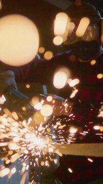 Man working at factory cuts metal, vertical. Male at a construction site cuts off piece, bright flying sparks and particles of material fly. Guy Industrial worker use angle grinder cutting metal