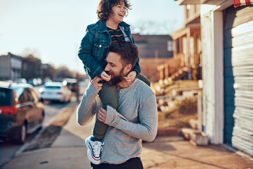 Fototapeta premium Father giving child a shoulder ride on a suburban street