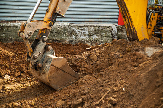 Excavator tractor bucket digging the ground at a construction site. Three-Jointed Boom Bucket Holder