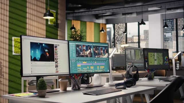 Empty office with no people featuring powerful PC dual monitors, displaying professional film editing software. Cinematic video project timeline with raw clips and cutting tools, media industry.