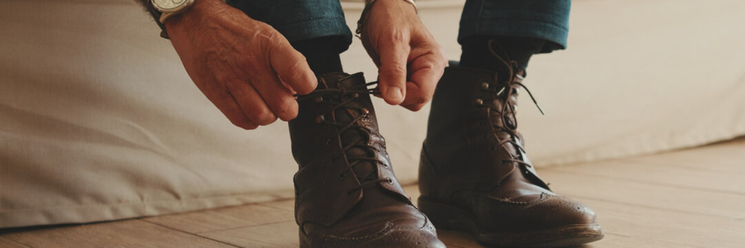 Close-up of legs of mature man putting on casual boots, tying shoelaces. Panoramic