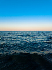 Obraz premium Sunset over the ocean with blue sky and calm water at the horizon viewed from the shore during the evening