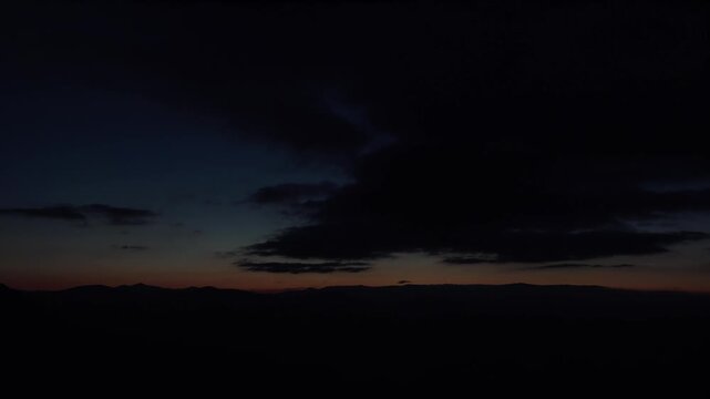 Timelapse of cloudy sky before sunrise at end of night with dark predawn atmosphere. Dawn cloudscape drifts through twilight gloom into warm morning color above a calm scene.