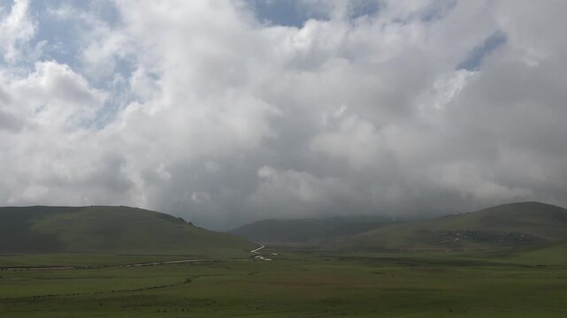 Time lapse clouds drift above treeless hill grasslands covered with vivid green summer growth. Moving sky reveals rolling plains open terrain natural rhythm across remote russian land.