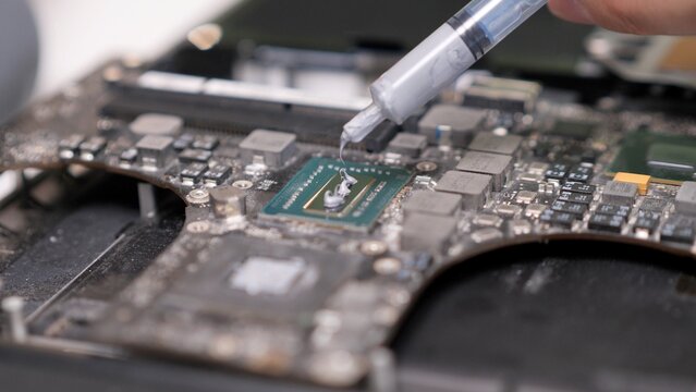 Hand applying thermal paste during laptop motherboard maintenance