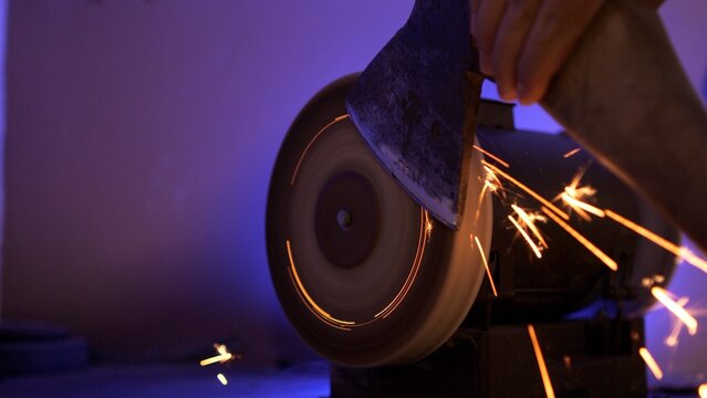 Person sharpening an axe on a bench grinder, creating metal sparks