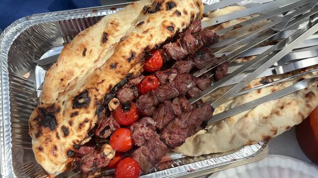 Grilled shashlik skewers with meat and cherry tomatoes served in toasted flatbread on a silver tray at an Israeli Independence Day picnic
