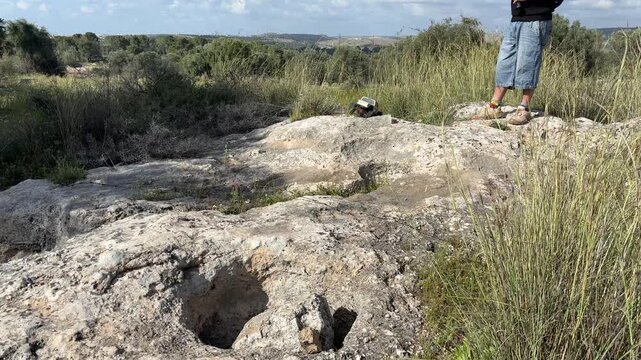 Person standing on rocky landscape with Mediterranean shrubs, remote control car outdoor terrain and adventure concept