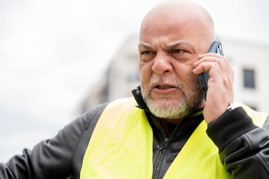 Bald man wearing safety vest yelling on phone