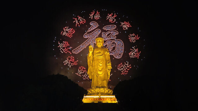 Big buddha statue of Lingshan. 
A photo of festive fireworks 
in night sky. Beautiful light show on
chinese new year eve. Grandiose carnival.
Golden religious sculpture.