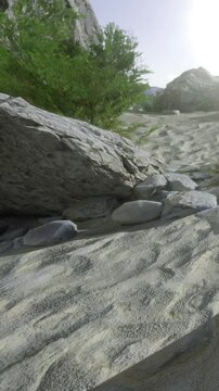 The sun sets over a dry riverbed filled with rocks and stones. Plants grow along the banks as the warm light highlights the textures of the stones and the surrounding landscape.