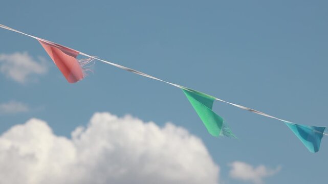 Colorful party pennants blowing in wind against blue sky with clouds