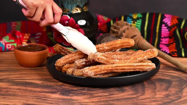 Hands placing a freshly fried churro onto a plate using silicone tongs. Mexican background