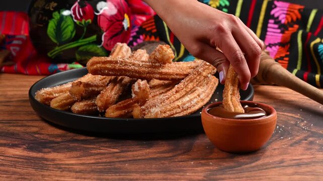 Woman's hand dipping a churro into a clay bowl filled with cajeta (caramelized milk)