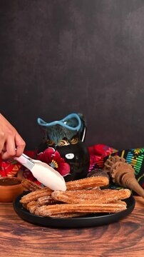 Hands placing a freshly fried churro onto a plate using silicone tongs