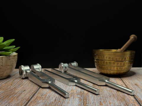 Set of Metal Tuning Forks with Singing Bowl and Succulent Plant on Wooden Table for Sound Healing Meditation Wellness Therapy Holistic Vibration Frequency Concept with Dark Background