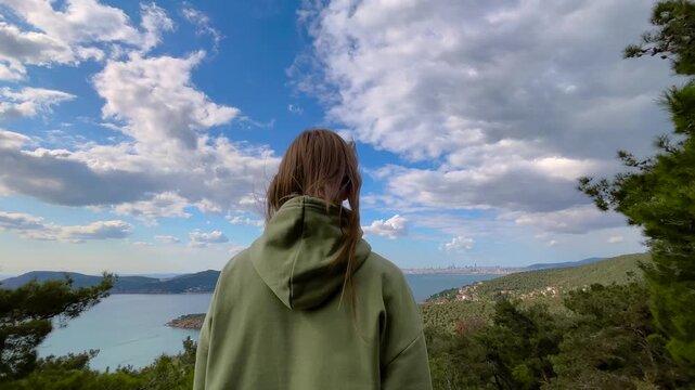 Back view of woman raising arms under wide sky while enjoying sea and island view near Istanbul. Freedom, openness and travel lifestyle concept