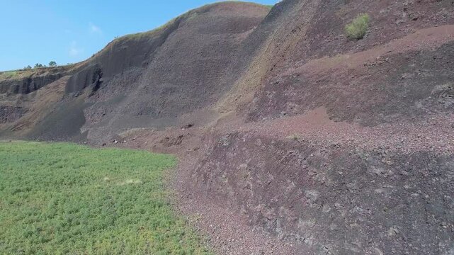 Aerial volcanic tuff cone layers reveal exposed mineral bands and rugged geologic structure. Eroded ash deposits, raw stratification, ancient eruption traces show striking earth history.