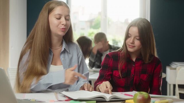 Happy joyful Caucasian teen girls talking discussing book with classmate lesson in classroom school education learning schoolgirls teenagers friendship study cooperation students reading literature