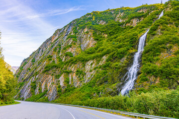 Tall waterfall cascades down a lush mountainside beside a winding road at Thompson Pass near Valdez, Alaska. © ZL Visuals